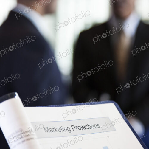 A closeup view of a business report with two businessmen in the background. A closeup view of a business report with two businessmen in the background.