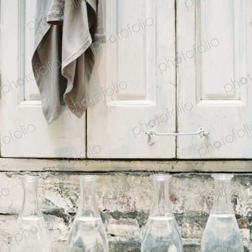 A cloth hanging from a peg on a a cupboard door, above a shelf of glass carafes.