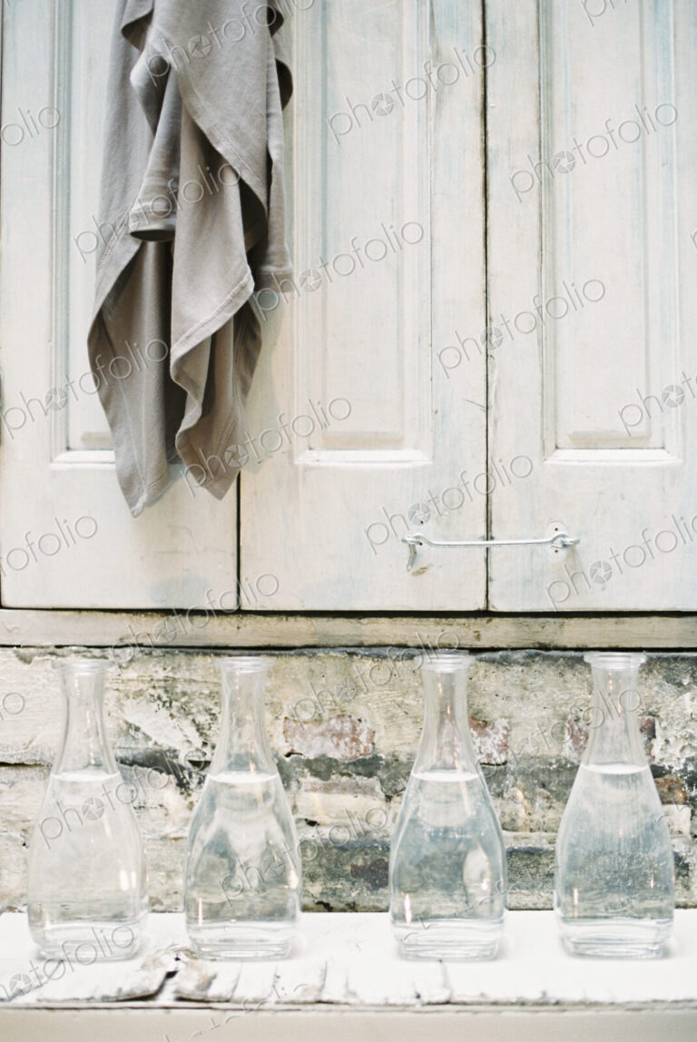 A cloth hanging from a peg on a a cupboard door, above a shelf of glass carafes.