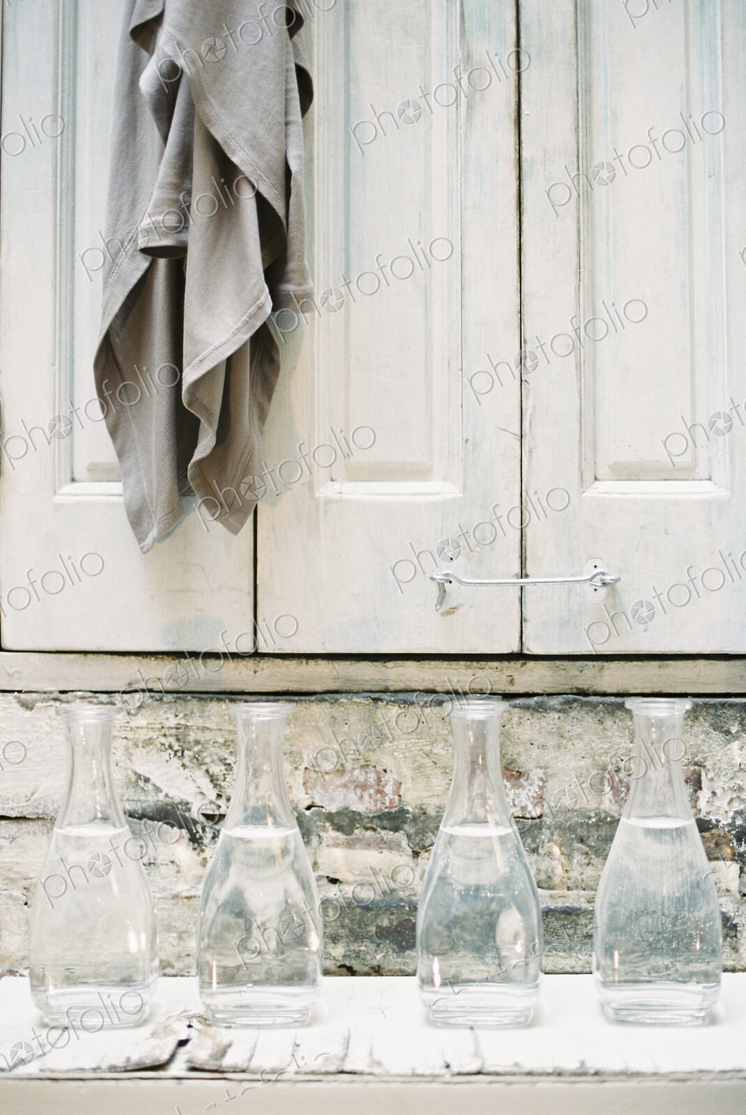 A cloth hanging from a peg on a a cupboard door, above a shelf of glass carafes.