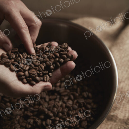 A coffee shop. A person holding a handful of fresh roasted coffee beans.