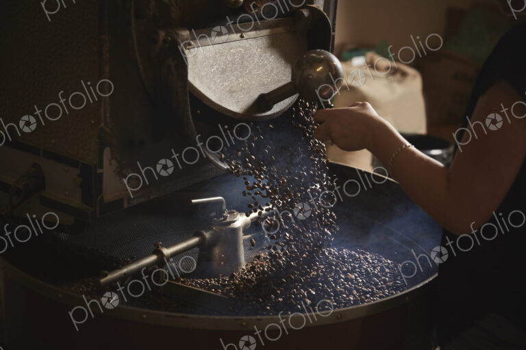 A coffee shop. A person opening a metal shute and coffee beans falling into a roasting…