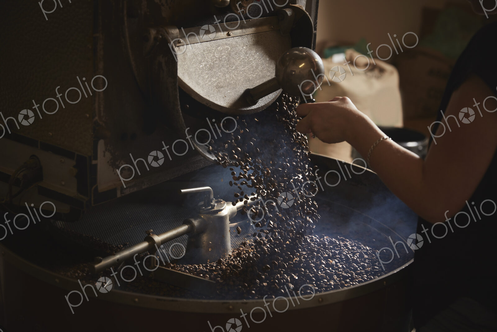 A coffee shop. A person opening a metal shute and coffee beans falling into a roasting…