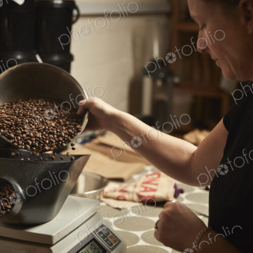 A coffee shop. A person pouring roasted coffee beans into a coffee grinder. A coffee shop. A person pouring roasted coffee beans into a coffee grinder.