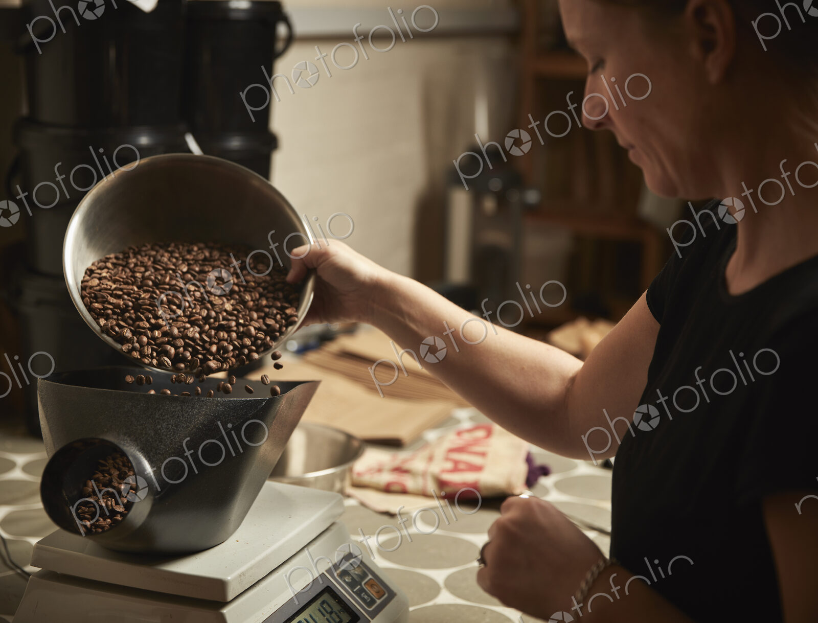 A coffee shop. A person pouring roasted coffee beans into a coffee grinder.