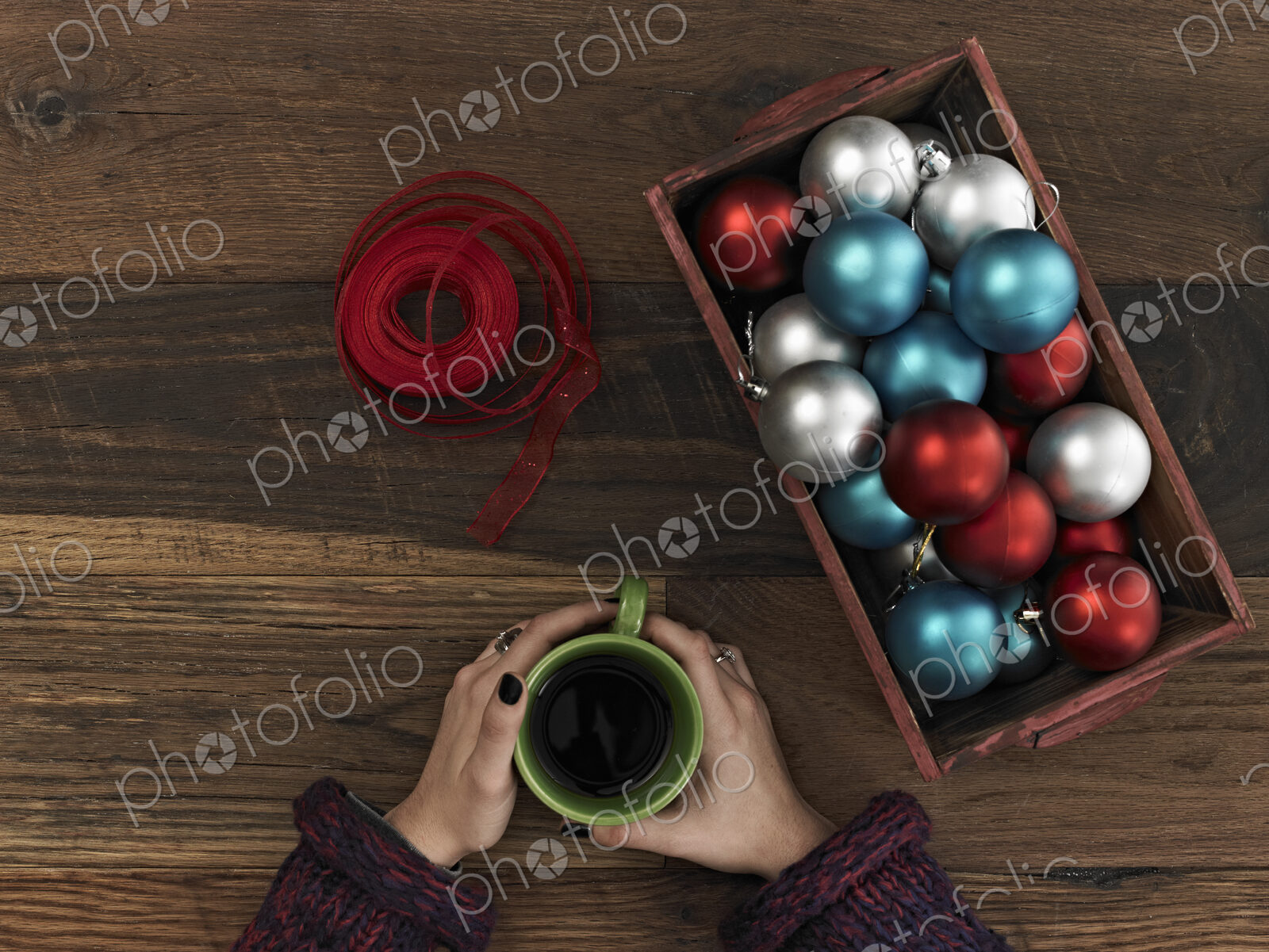 A collection of blue, red and silver ornaments and red ribbon in a box on a wooden…