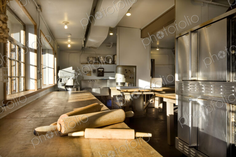 A commercial bakery with row of ovens and preparation area, a wooden board with three…