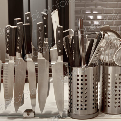 A commercial kitchen worktop, rows of knifes on a magnetic strip and utensils in pots. A commercial kitchen worktop, rows of knifes on a magnetic strip and utensils in pots.