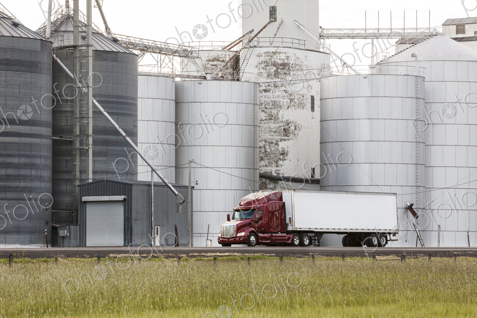 A commercial truck driving past grain elevators in the farm country of eastern…