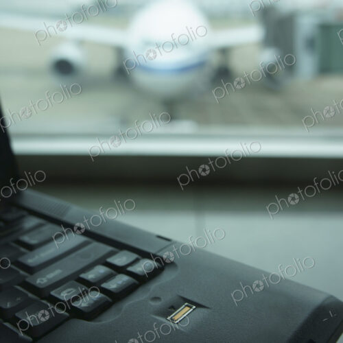 A computer laptop on a surface,in front of a window. Airport apron and aircraft seen… A computer laptop on a surface,in front of a window. Airport apron and aircraft seen…