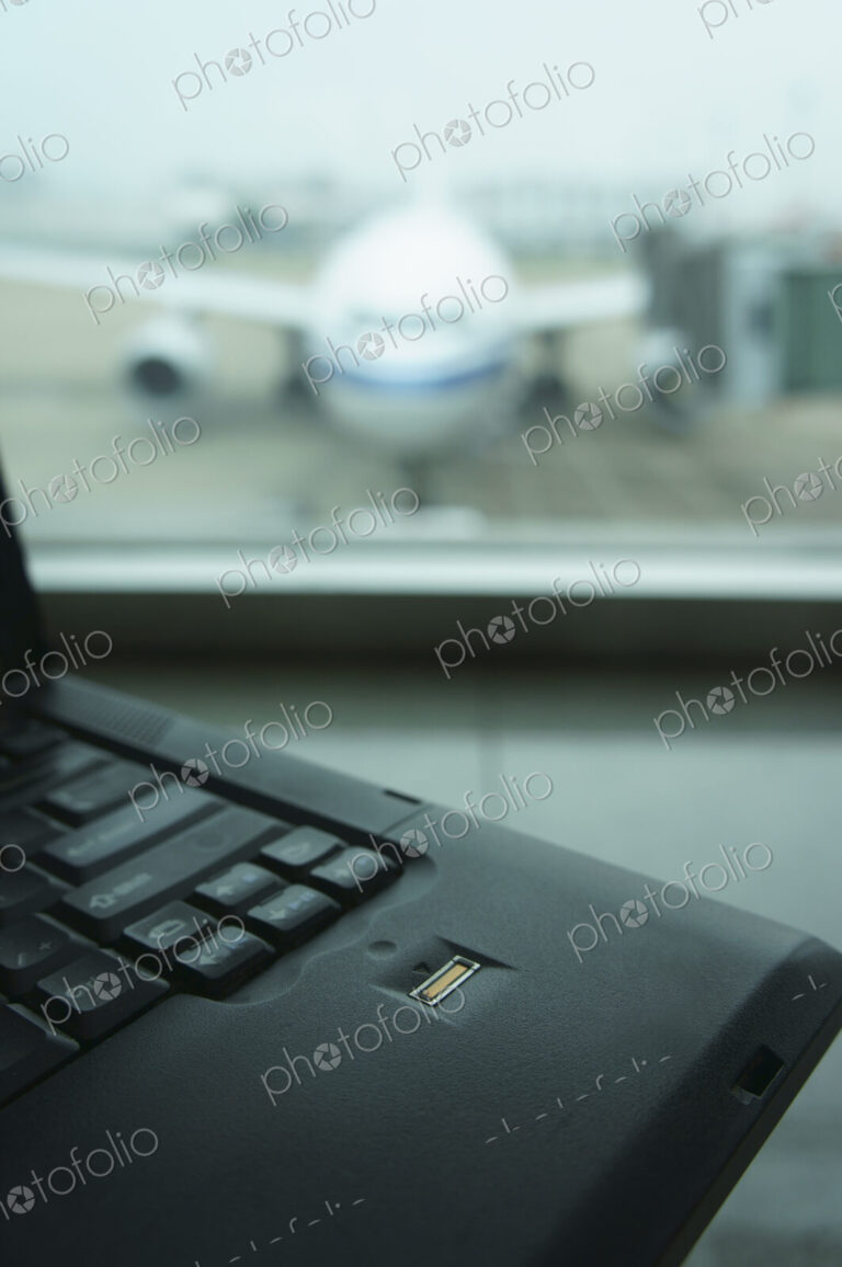 A computer laptop on a surface,in front of a window. Airport apron and aircraft seen…