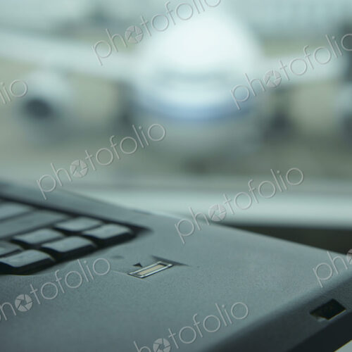 A computer laptop on a surface,in front of a window. Airport apron and aircraft seen… A computer laptop on a surface,in front of a window. Airport apron and aircraft seen…