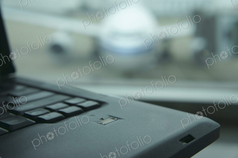 A computer laptop on a surface,in front of a window. Airport apron and aircraft seen…