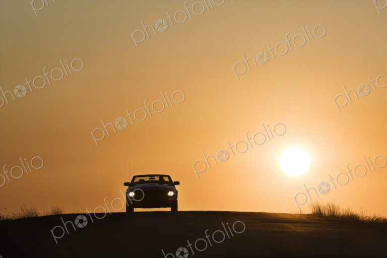 A convertible sports car on a country highway at sunset.