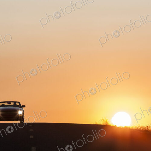 A convertible sports car on a country highway at sunset.