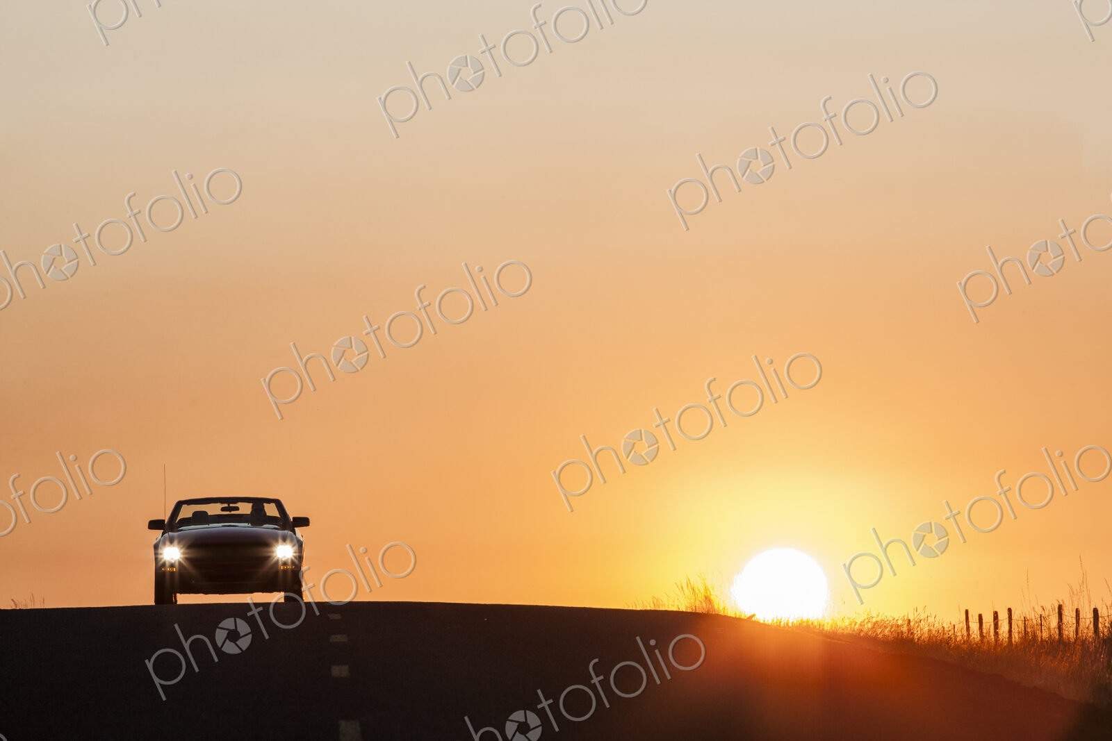A convertible sports car on a country highway at sunset.