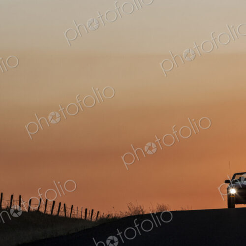A convertible sports car on a country highway at sunset.