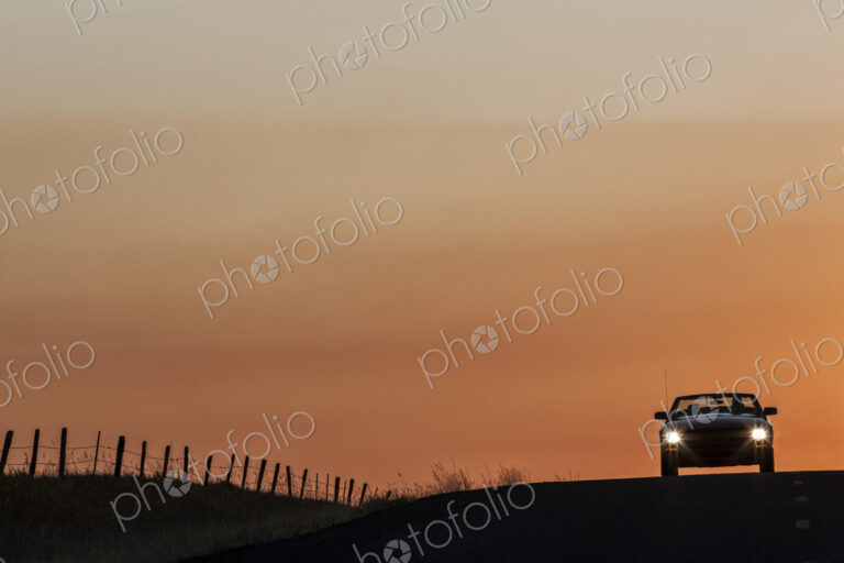 A convertible sports car on a country highway at sunset.
