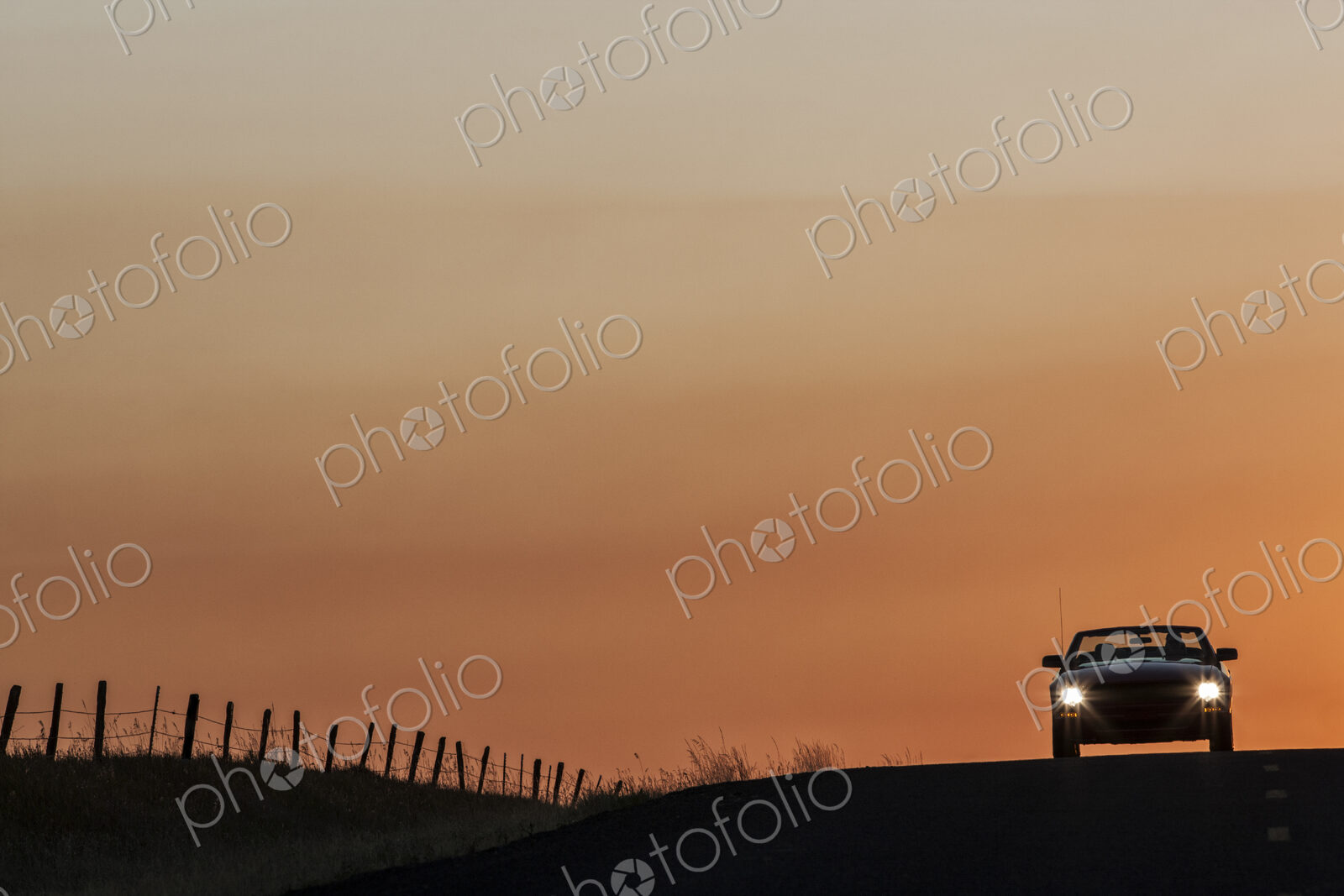 A convertible sports car on a country highway at sunset.