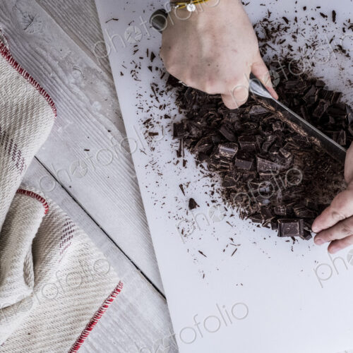A cook chopping chocolate pieces with a large cleaver. A cook chopping chocolate pieces with a large cleaver.