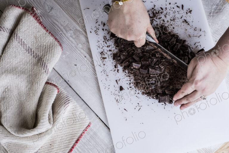A cook chopping chocolate pieces with a large cleaver.