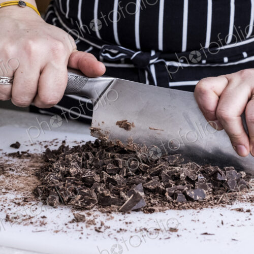 A cook chopping chocolate pieces with a large cleaver. A cook chopping chocolate pieces with a large cleaver.