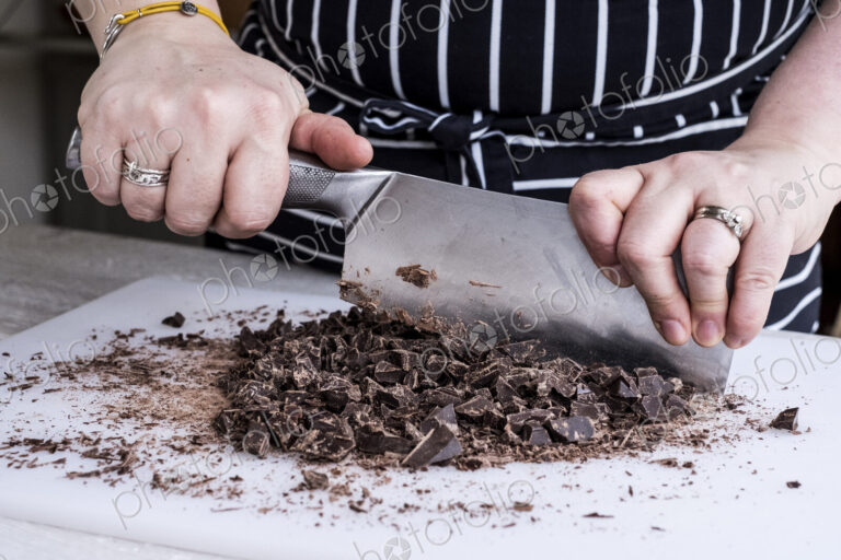 A cook chopping chocolate pieces with a large cleaver.
