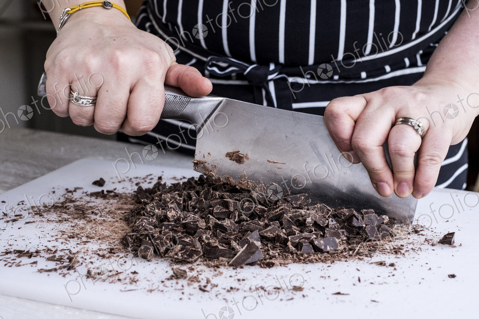 A cook chopping chocolate pieces with a large cleaver.