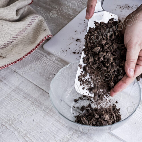 A cook holding a cleaver blade with chopped chocolate pieces. A cook holding a cleaver blade with chopped chocolate pieces.