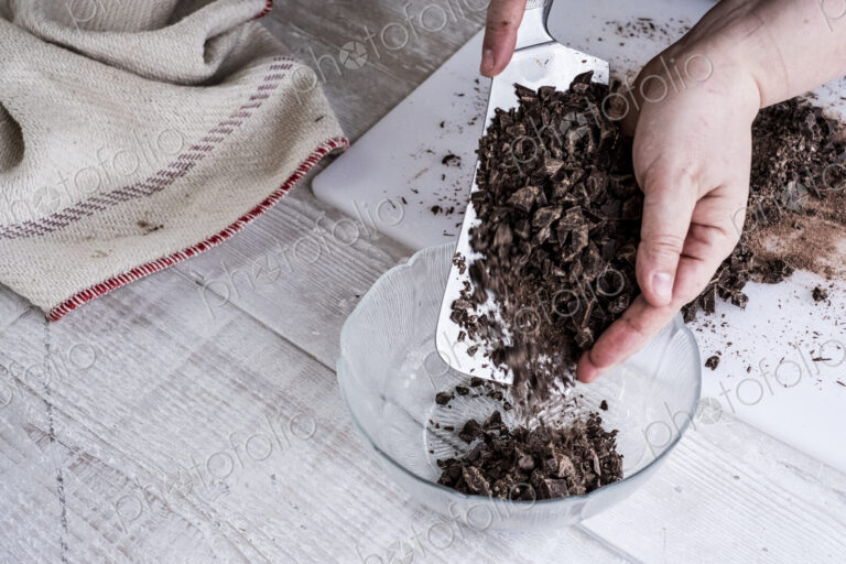 A cook holding a cleaver blade with chopped chocolate pieces.
