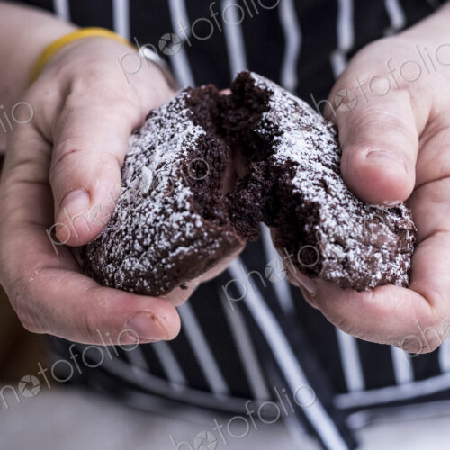 A cook in an apron holding a dark chocolate brownie cake broken in half