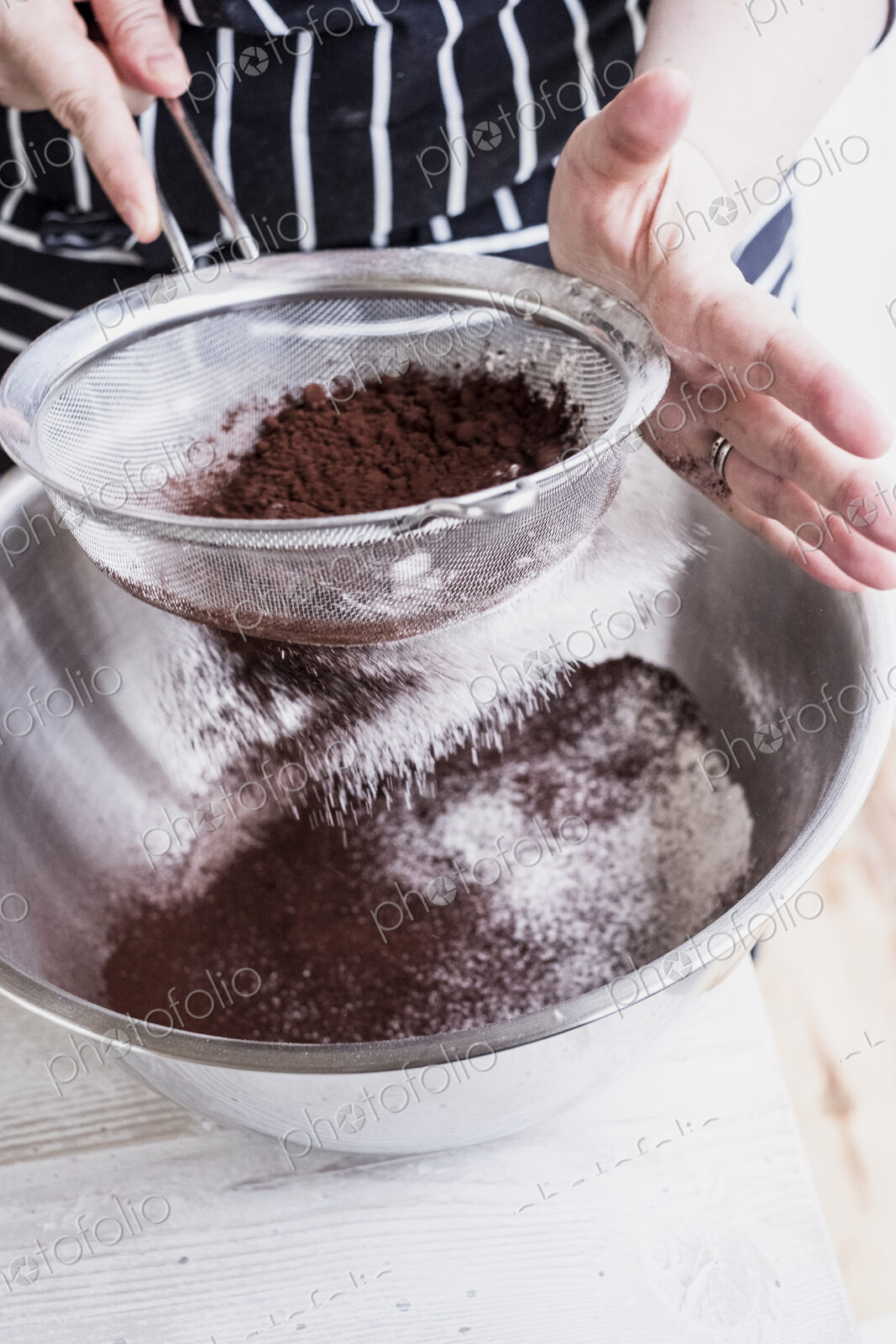 A cook sieving cocoa powder into a metal bowl of flour and cake ingredients.