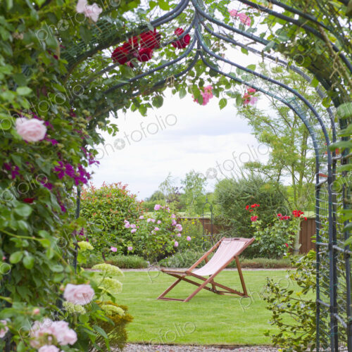 A country garden with a rose arch, and flowering climbing roses.