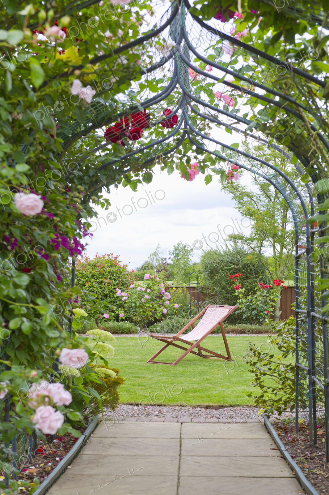 A country garden with a rose arch, and flowering climbing roses.