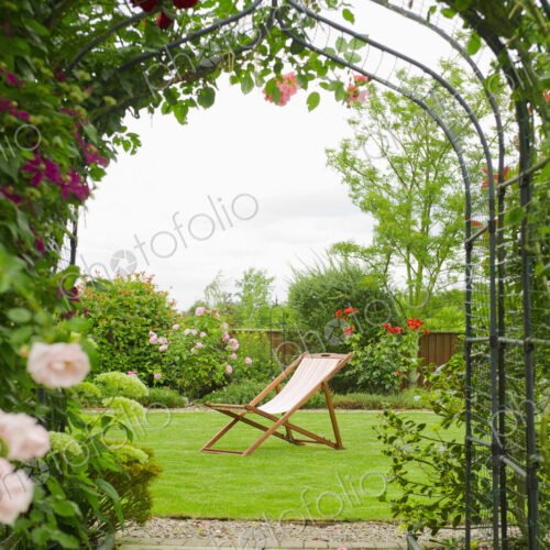 A country garden with a rose arch, and flowering climbing roses.
