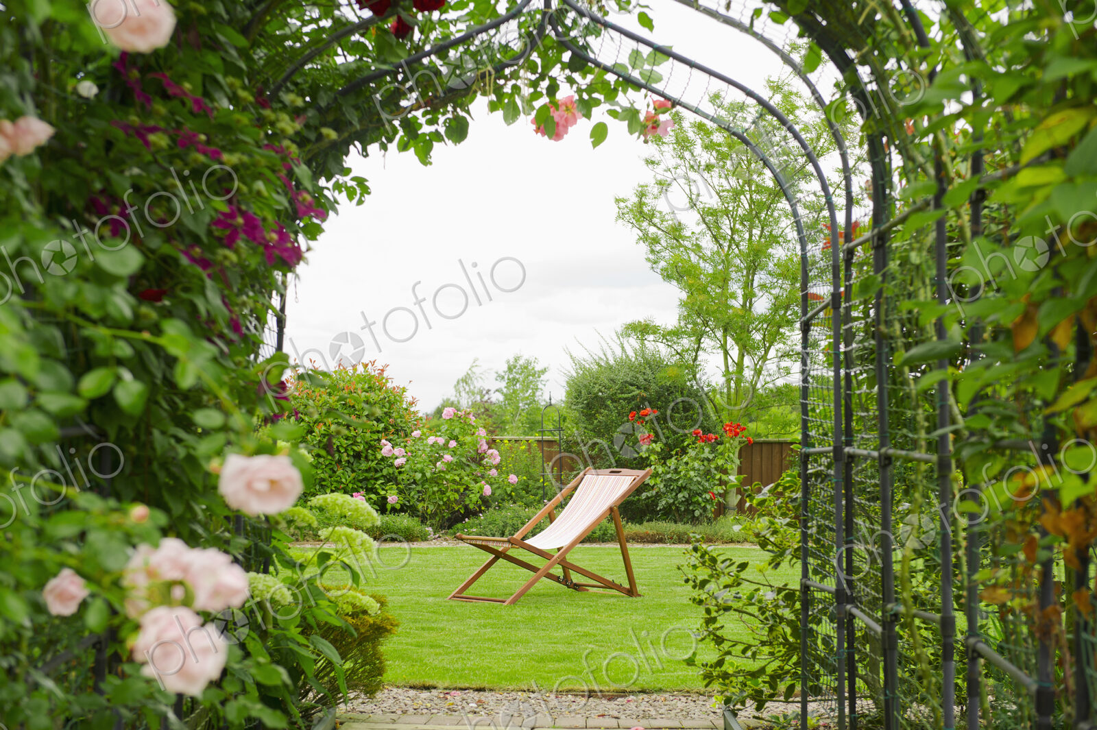 A country garden with a rose arch, and flowering climbing roses.
