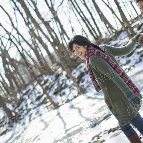 A couple hand in hand, on a snowy path through the woods.