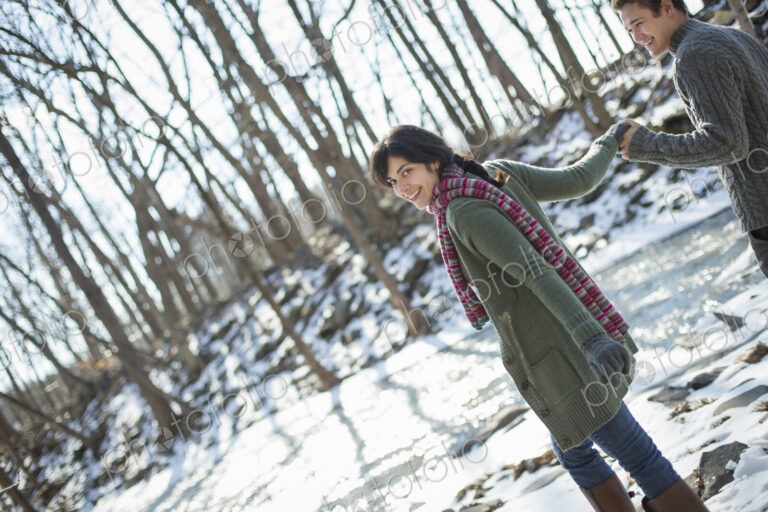A couple hand in hand, on a snowy path through the woods.