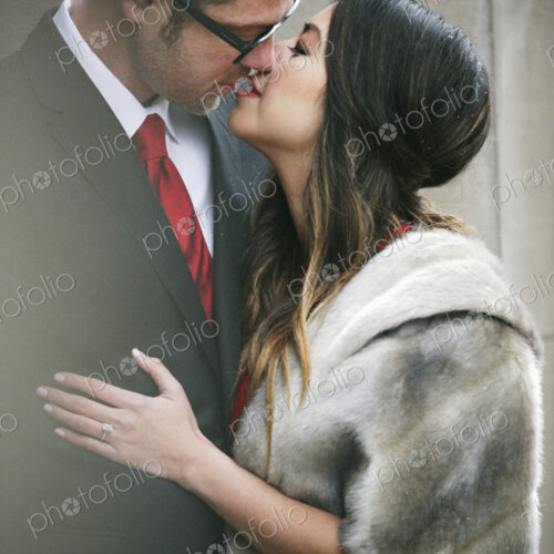 A couple in evening dress, a man and woman kissing on the street in a city.