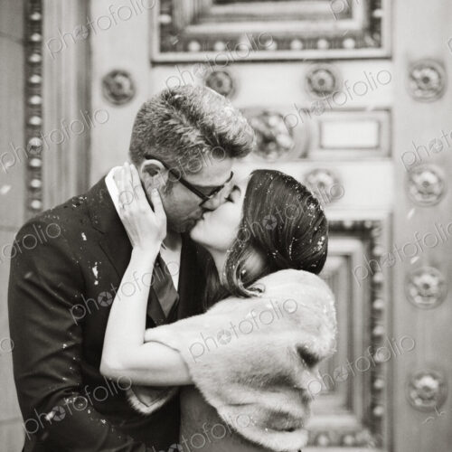 A couple in evening dress, a man and woman kissing on the street in a city.