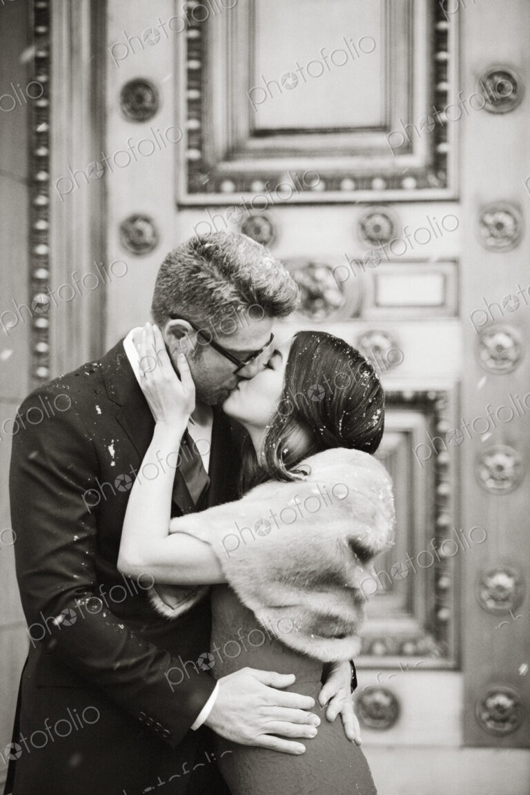 A couple in evening dress, a man and woman kissing on the street in a city.