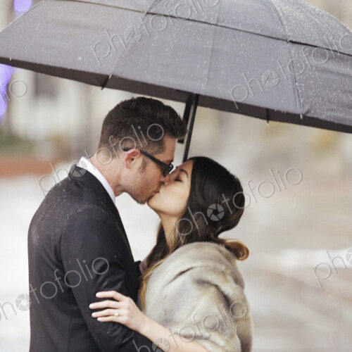 A couple in evening dress, a man and woman kissing under an umbrella.