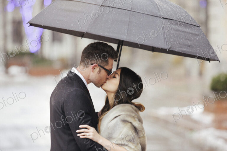 A couple in evening dress, a man and woman kissing under an umbrella.
