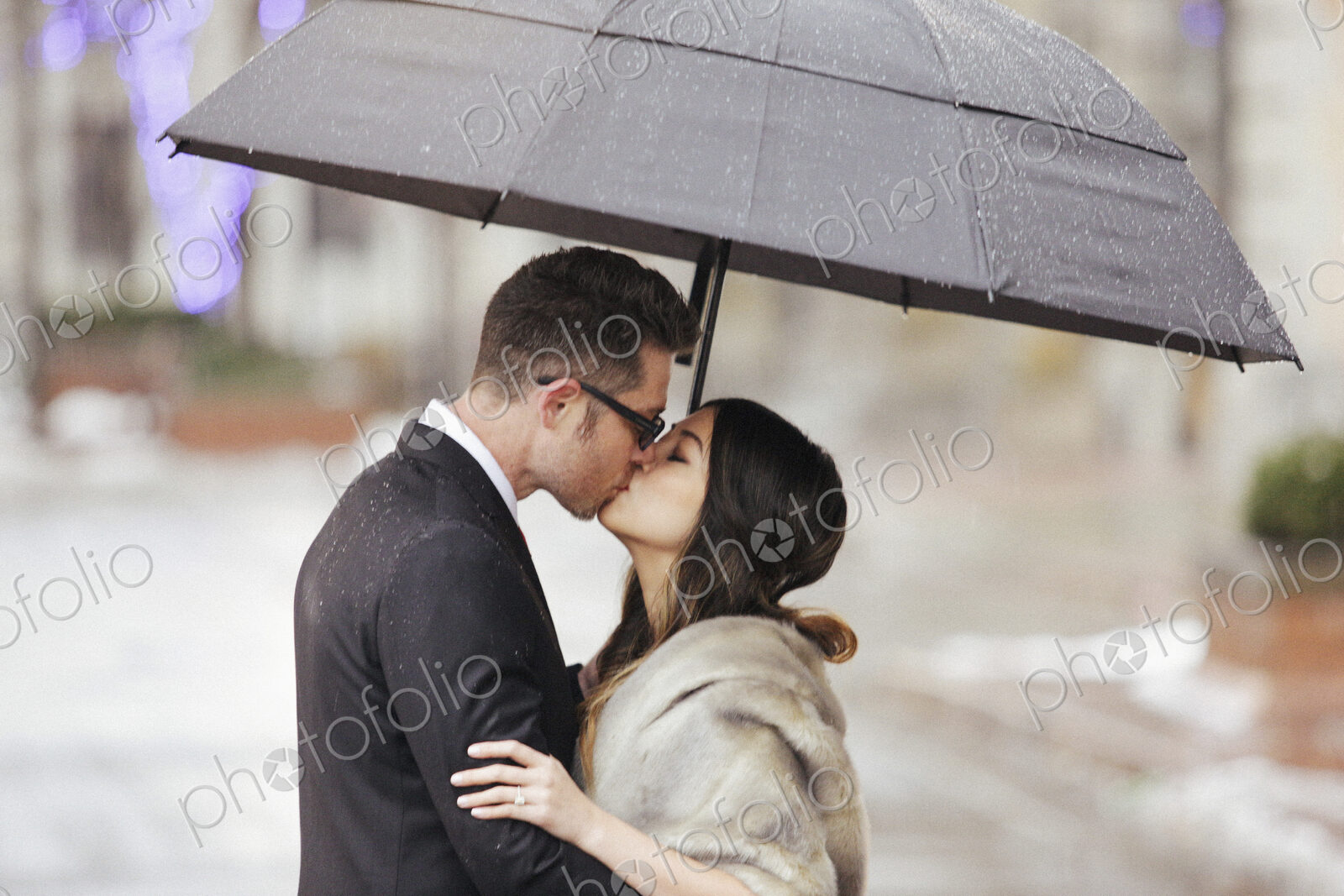 A couple in evening dress, a man and woman kissing under an umbrella.