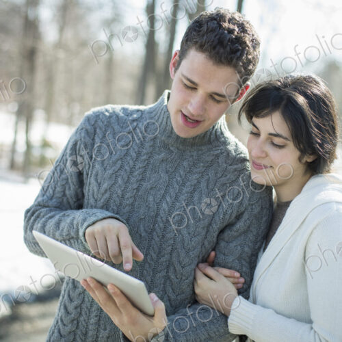 A couple looking at a computer tablet. Standing close together on a winter day in the…