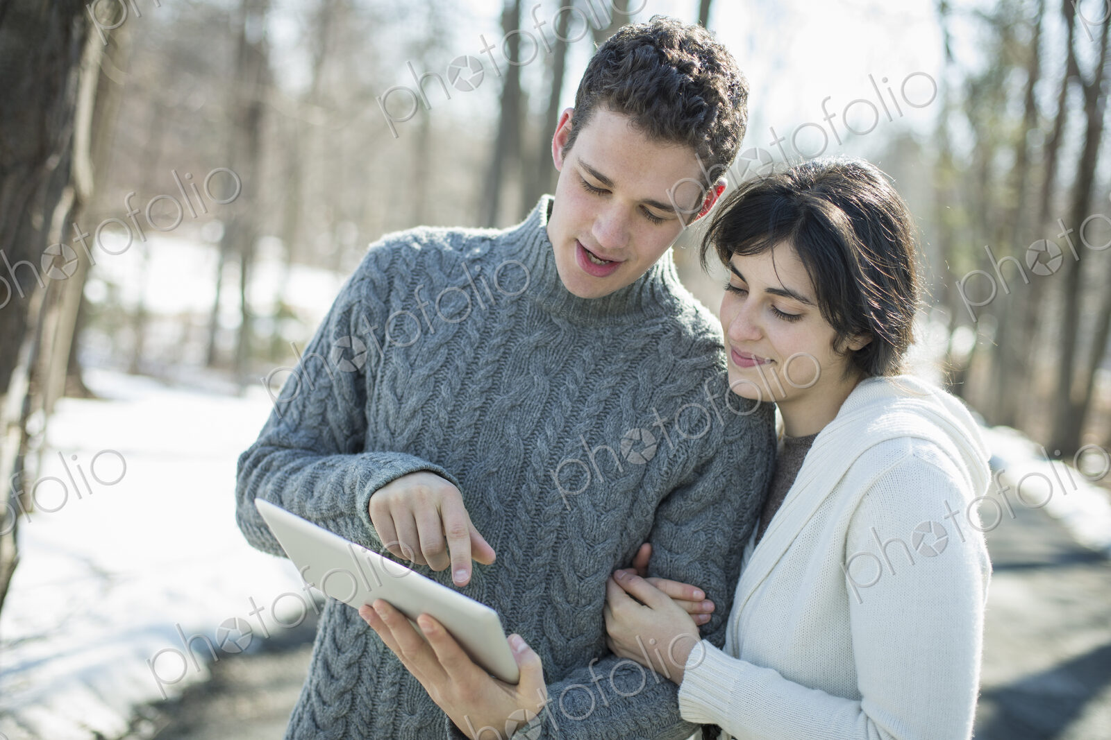 A couple looking at a computer tablet. Standing close together on a winter day in the…