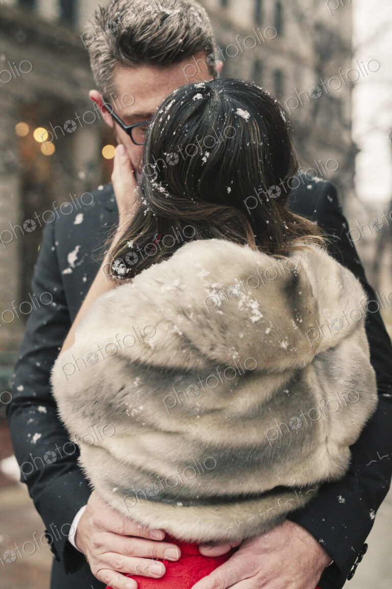 A couple, lovers kissing in lightly fall ing snow in the city.