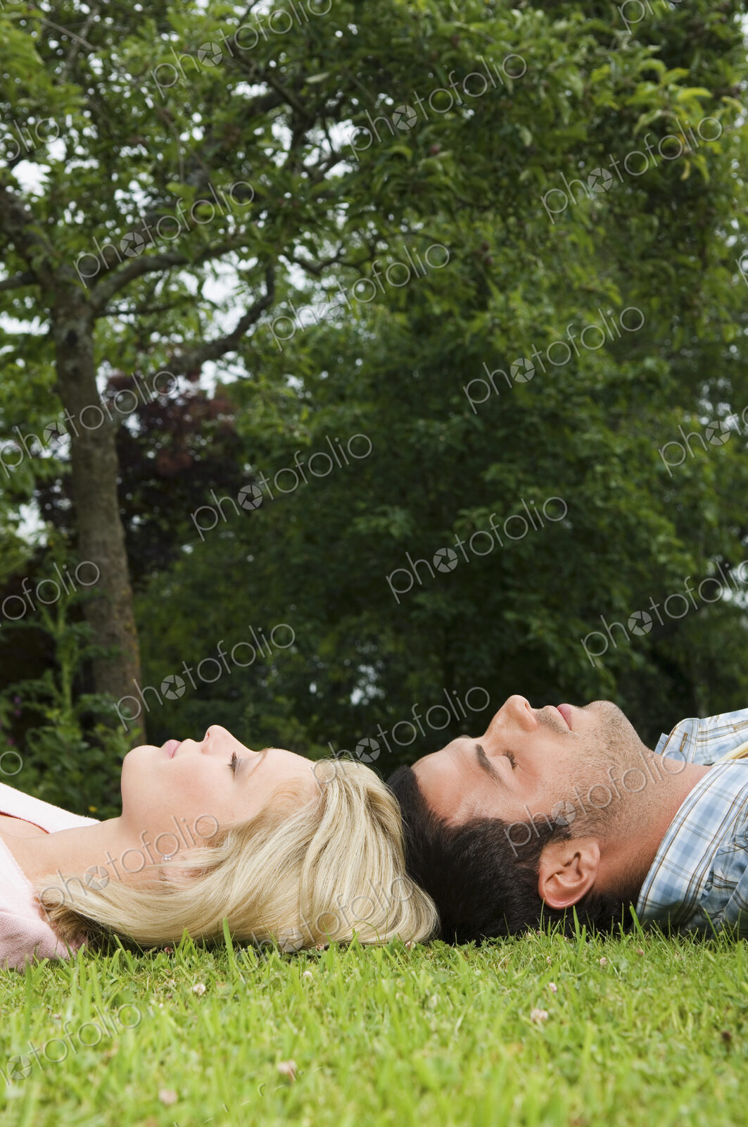 A couple lying on their backs, head touching on the grass,