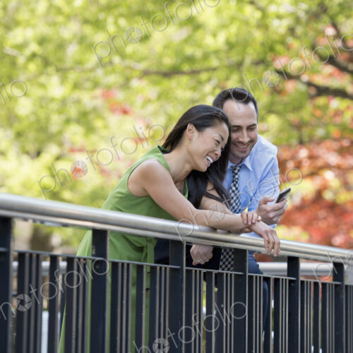A couple, man and woman checking a smart phone, under the shade of trees in the park. A couple, man and woman checking a smart phone, under the shade of trees in the park.