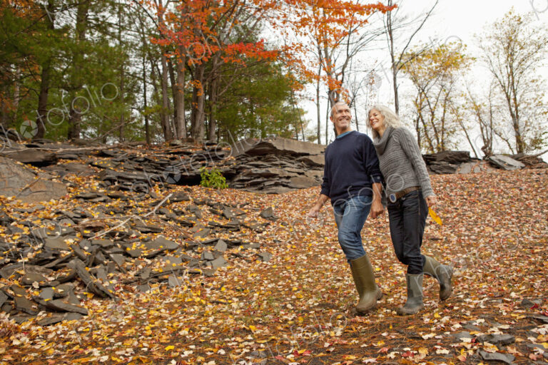 A couple, man and woman on a day out in autumn walking through fallen leaves. Holding…
